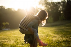 boy wearing striped shirt piggybacking on woman wearing in park at golden hour