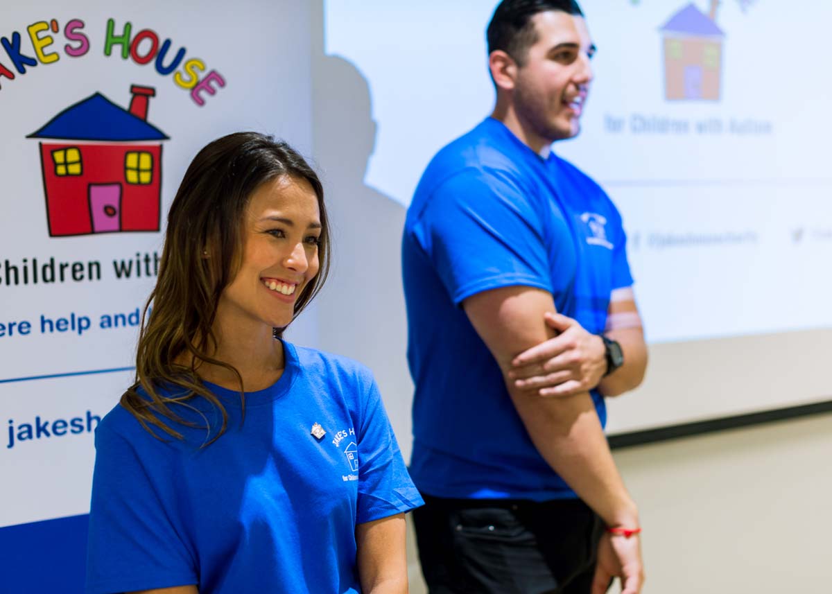 two people smiling in front of a display for Jake's House