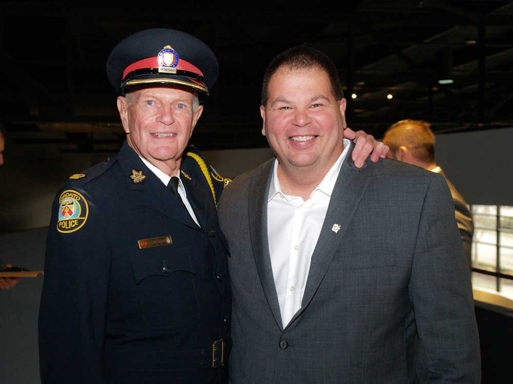 older police officer in uniform with arm on shoulder of man in grey suit smiling