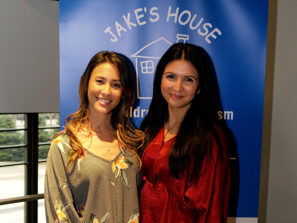 two smiling women in front of blue jake's house banner