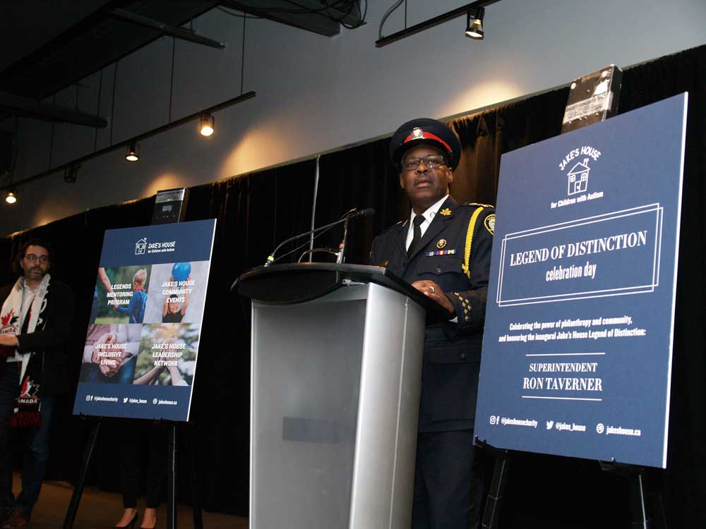 police officer in uniform standing at podium with two jake's house signs on each side