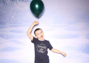 Boy with an expression of excitement holding a green balloon at a holiday party photo booth