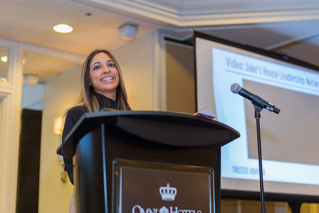 a smiling woman speaking from behind a podium in a conference room