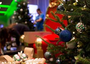Close up of a christmas tree with a blue and silver ornaments while a holiday party goes on in the background