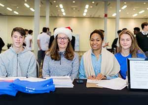 Four Jake's House volunteers sit at a registration table at a holiday charity event.
