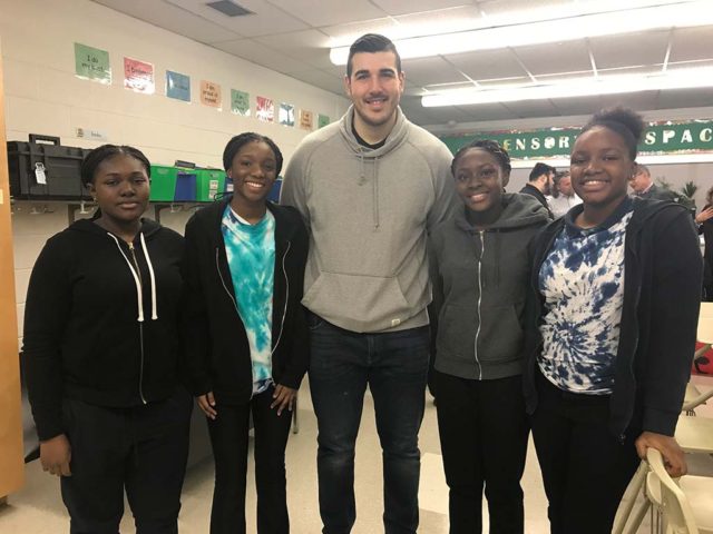 a tall man posing for a picture with four students in a classroom