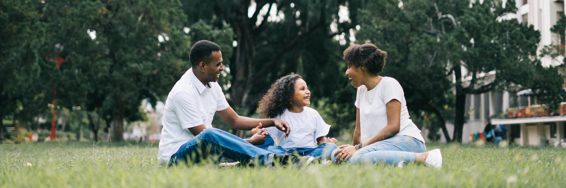 family of mom, dad and young daughter sitting on grass laughing