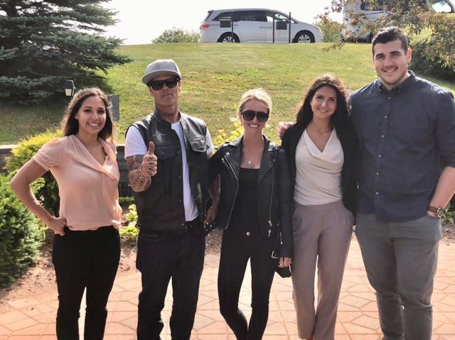 Five people posing and smiling outdoors on a sunny day