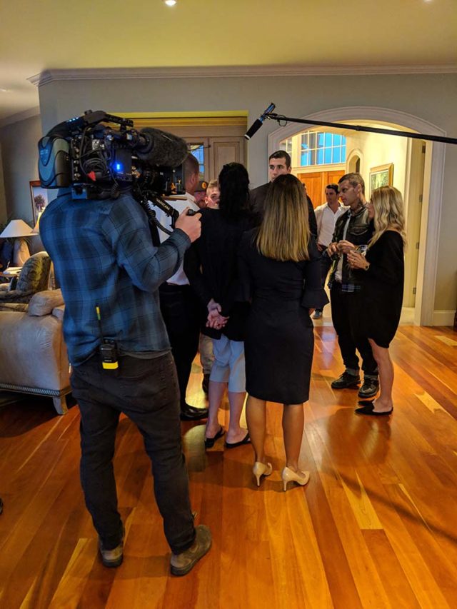 A film crew filming a group of formally dressed people in a reception room
