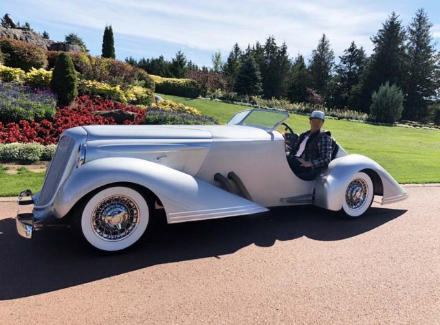 Bad Chad posing and smiling in a silver custom hot rod car on a sunny day