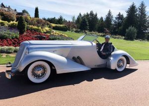 Bad Chad posing and smiling in a silver custom hot rod car on a sunny day