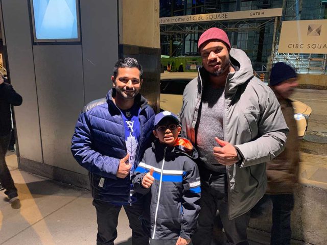 A boy and two men in winter clothes smiling and giving a "thumbs up" at a hockey game