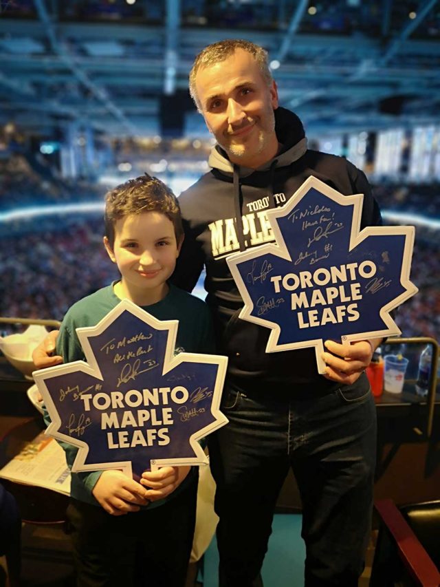 A man and a boy holding Toronto Maple Leafs cutouts at a hockey game