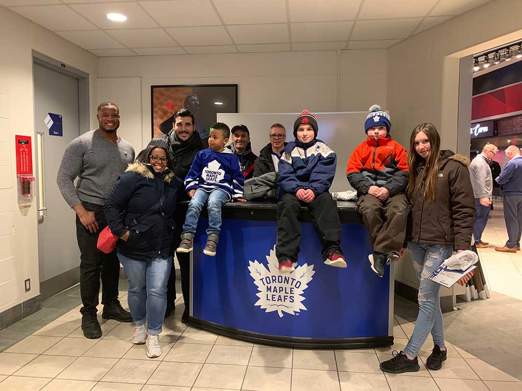 A group of people in winter clothes posing around a Toronto Maple Leafs branded desk