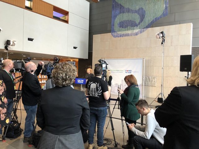 news cameras focused on a woman making an announcement at a press release