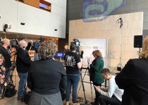 news cameras focused on a woman making an announcement at a press release