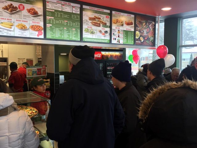 People in winter-wear line up for food at the grand opening of a new pizza shop