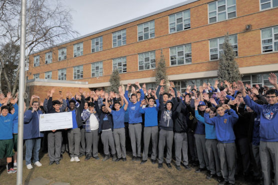 a group of people posing outside with a giant-sized cheque for a charity donation