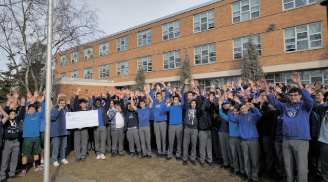 a group of people posing outside with a giant-sized cheque for a charity donation