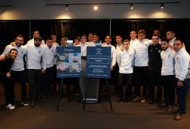 A group of people in white shirts with the same emblem on the breast posing at a charity event