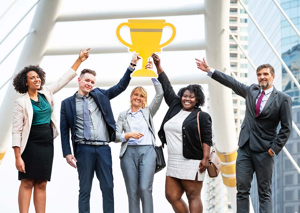 A group of office workers having fun and holding up a large paper trophy