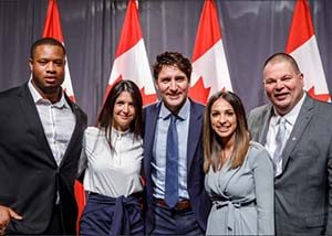 Four members of the Jake's House team posing with Prime Minister Justin Trudeau in front of Canadian flags
