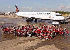 A large group of charity volunteers in red shirts posed outside an Air Canada plane on the tarmac