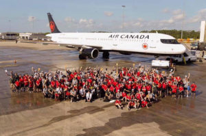 A large group of charity volunteers in red shirts posed outside an Air Canada plane on the tarmac