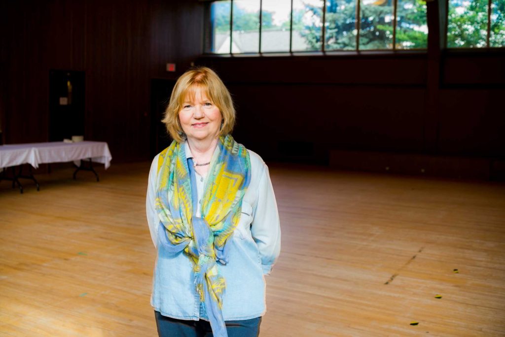 woman with blond hair wearing light blue shirt and scarf standing in gym