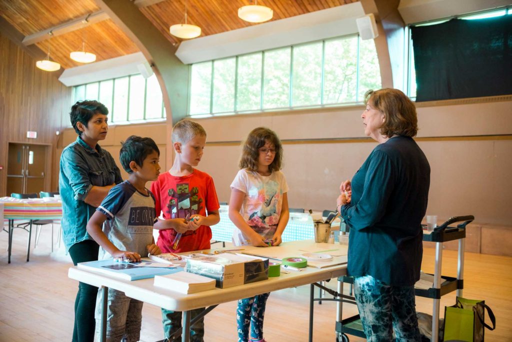 woman speaking in front of group of three children and woman in gymnasium