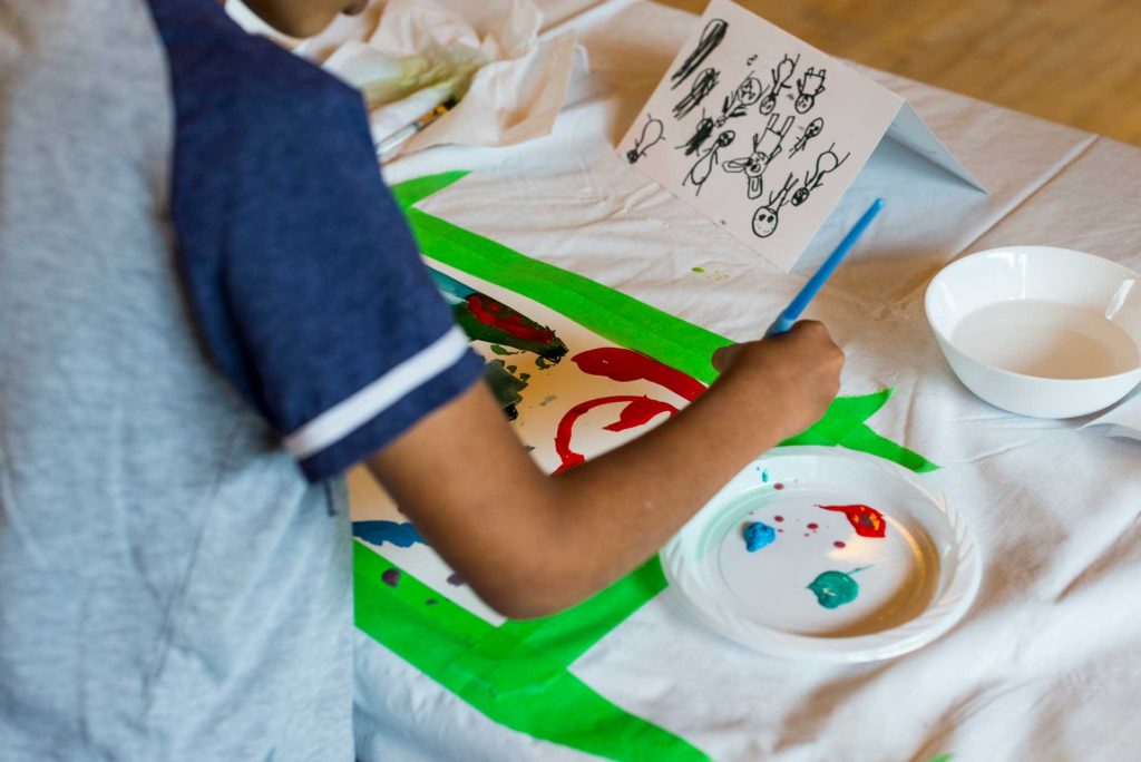 hand of child painting on paper taped to table