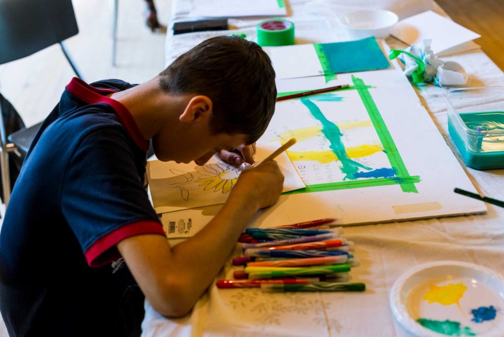 boy leaning forward over drawing of sunflower on table with pencil